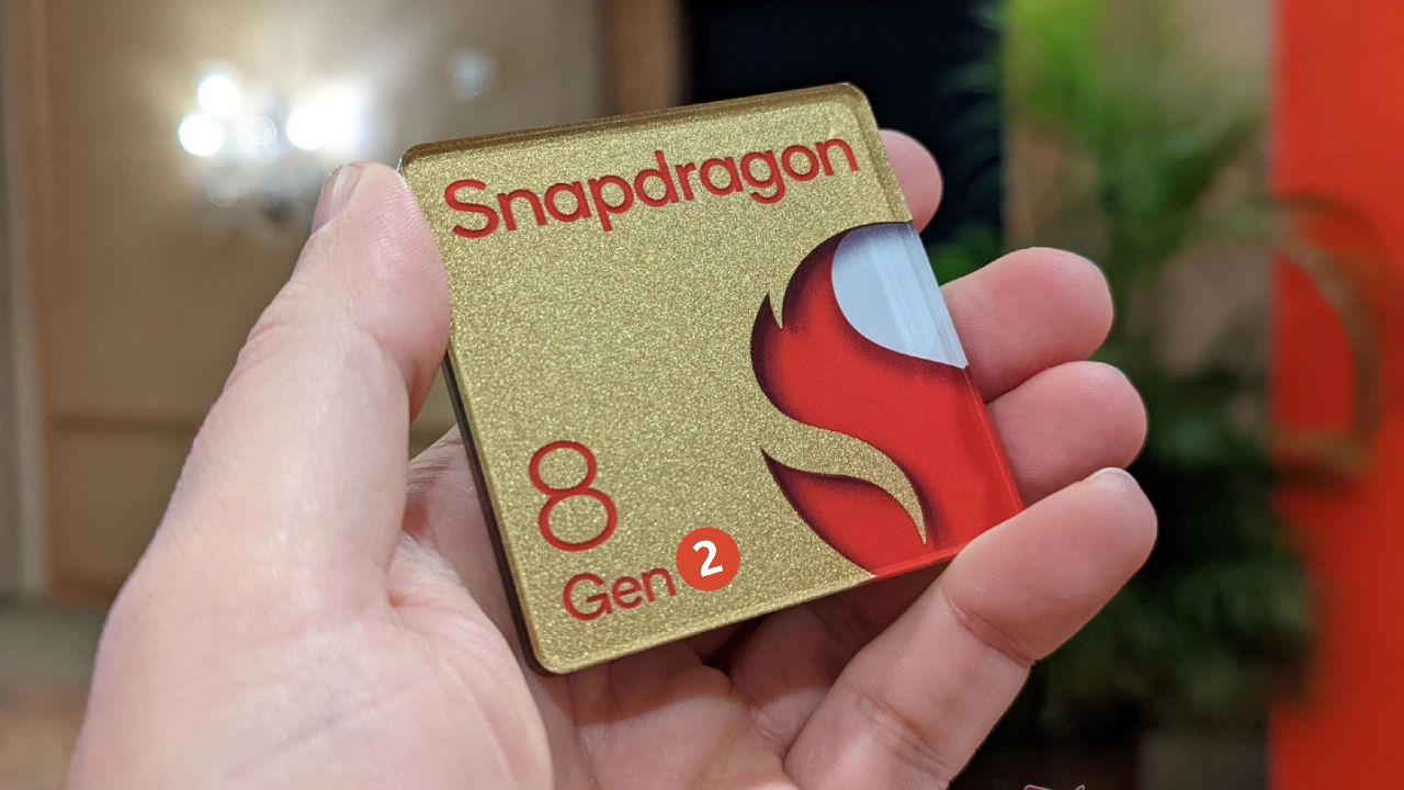  A hand holding a gold and red colored wafer with the Snapdragon 8 Gen 2 logo on it.